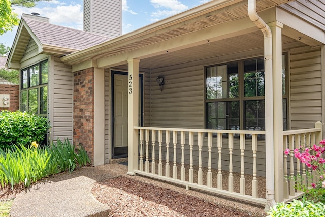 entrance to property featuring covered porch, brick siding, and a chimney