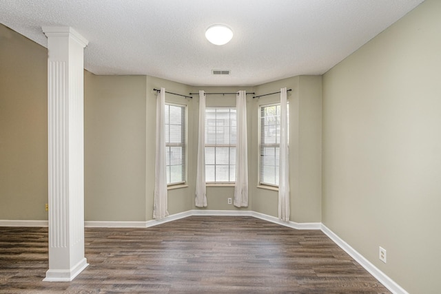 empty room featuring visible vents, a textured ceiling, dark wood-style flooring, and ornate columns