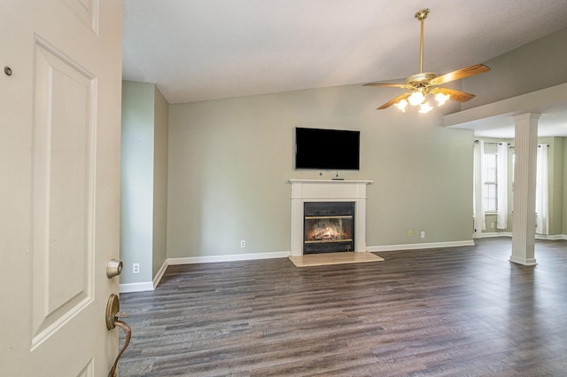 unfurnished living room featuring a glass covered fireplace, ceiling fan, decorative columns, and dark wood finished floors