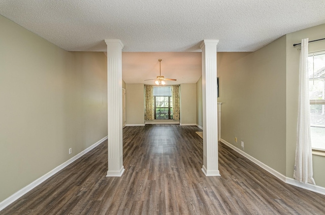 unfurnished dining area with baseboards, a ceiling fan, ornate columns, and dark wood-style floors