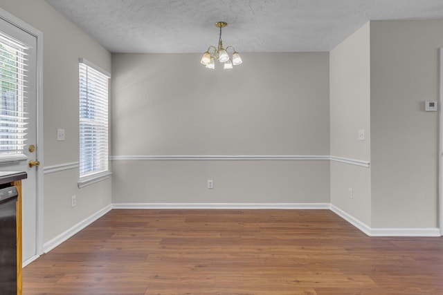 unfurnished dining area featuring an inviting chandelier, a textured ceiling, wood finished floors, and a healthy amount of sunlight