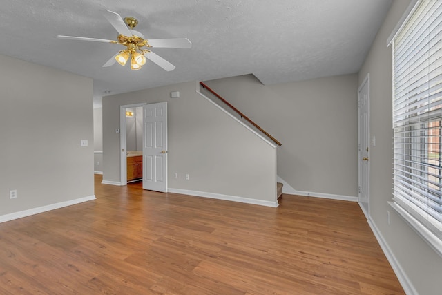 unfurnished living room with a ceiling fan, a textured ceiling, wood finished floors, stairway, and baseboards