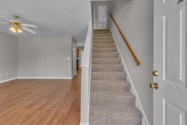 stairs featuring baseboards, a textured ceiling, ceiling fan, and wood finished floors