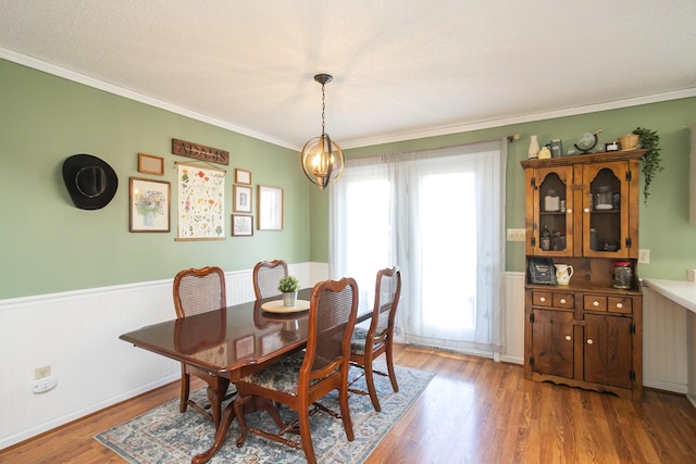 dining area with crown molding, a notable chandelier, light wood-type flooring, and a wainscoted wall