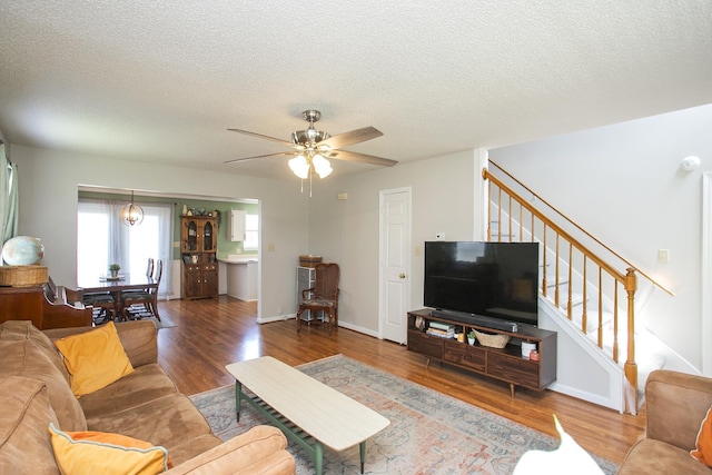 living area featuring ceiling fan, a textured ceiling, baseboards, wood finished floors, and stairway