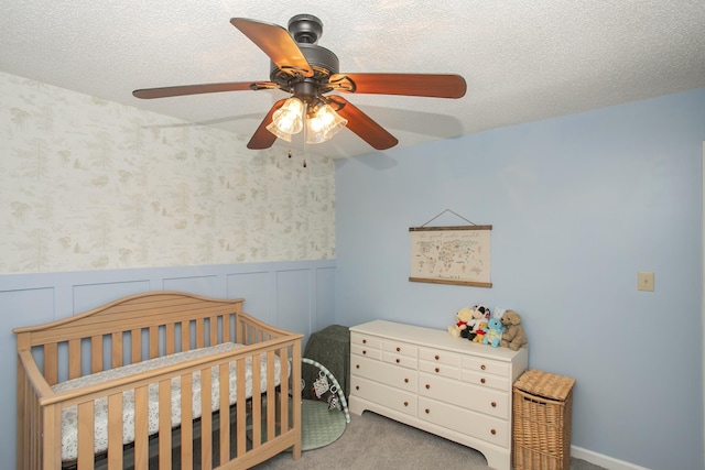 bedroom with carpet, a crib, a ceiling fan, and wainscoting
