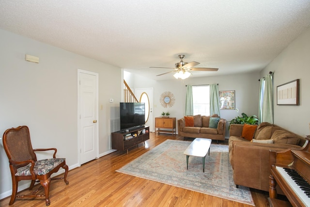 living room featuring baseboards, ceiling fan, stairway, a textured ceiling, and light wood-style flooring
