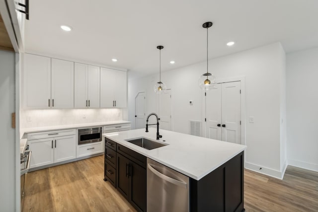kitchen featuring stainless steel dishwasher, white cabinetry, a sink, and light wood finished floors