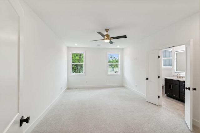 unfurnished bedroom with baseboards, ensuite bathroom, ceiling fan, light colored carpet, and a sink