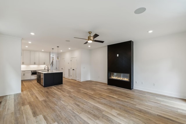 unfurnished living room featuring a sink, recessed lighting, and light wood-style flooring