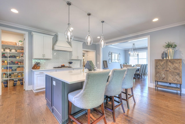 kitchen featuring white cabinets, ornamental molding, decorative backsplash, wood finished floors, and custom exhaust hood
