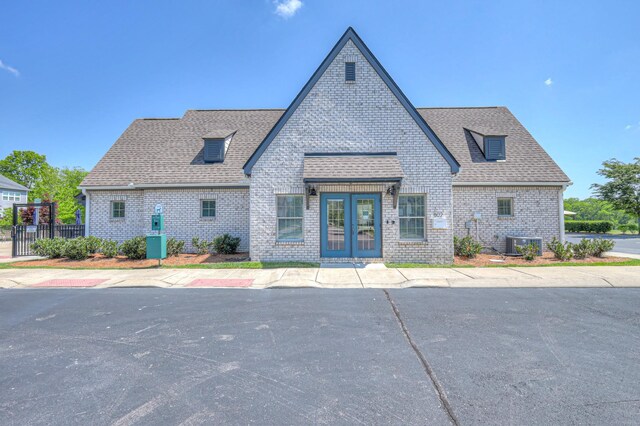 view of front of house featuring french doors, roof with shingles, brick siding, cooling unit, and fence