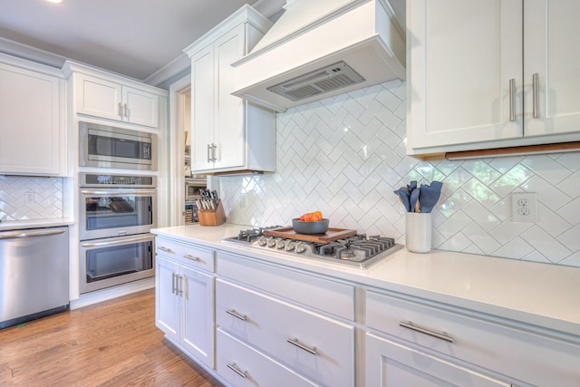 kitchen featuring backsplash, white cabinetry, appliances with stainless steel finishes, and custom range hood
