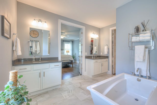 bathroom featuring a sink, a soaking tub, marble finish floor, and two vanities