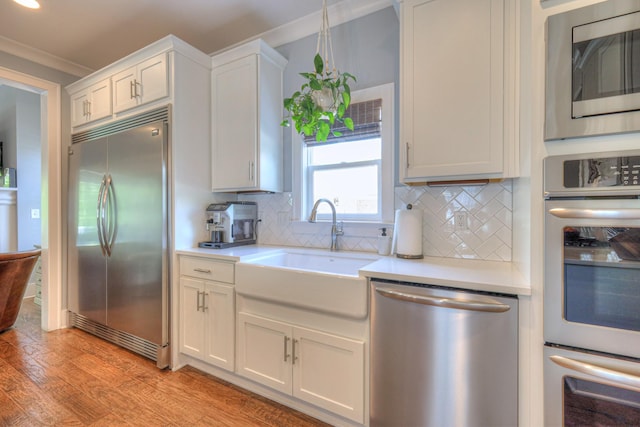 kitchen with built in appliances, decorative backsplash, a sink, and light countertops