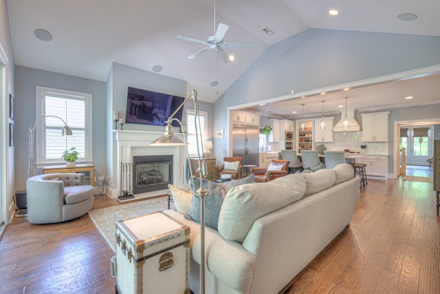 living area with a ceiling fan, recessed lighting, a fireplace with raised hearth, and light wood-style floors