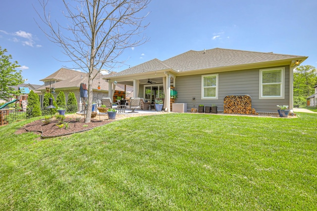 back of house featuring ceiling fan, a patio, roof with shingles, a playground, and a lawn
