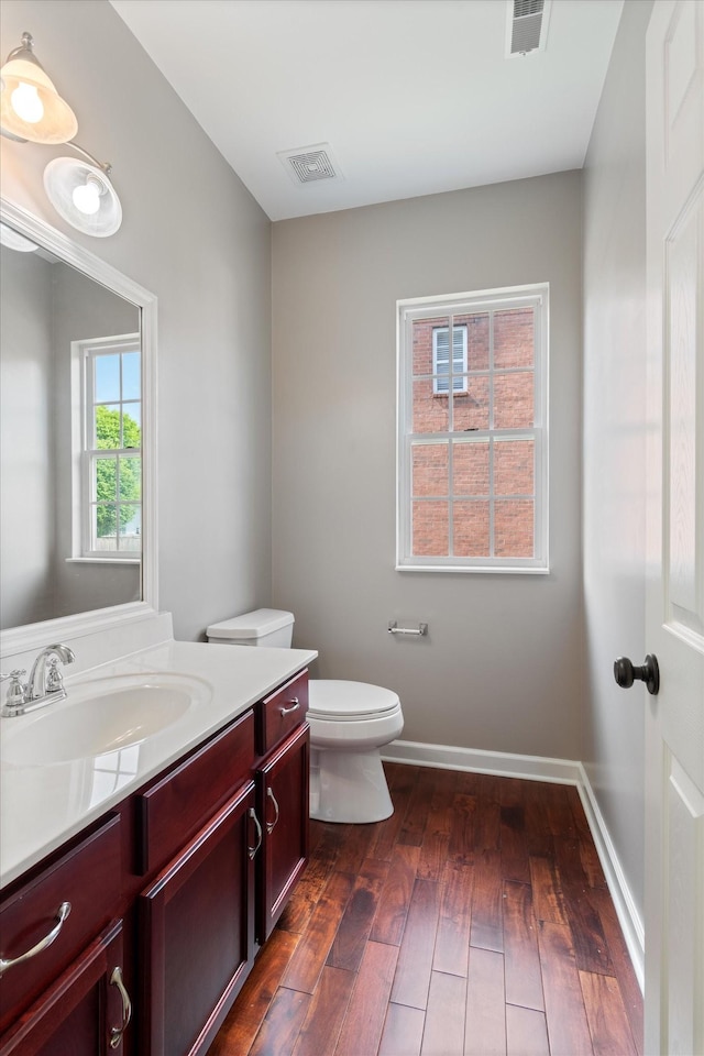 bathroom with hardwood / wood-style flooring, vanity, toilet, and visible vents