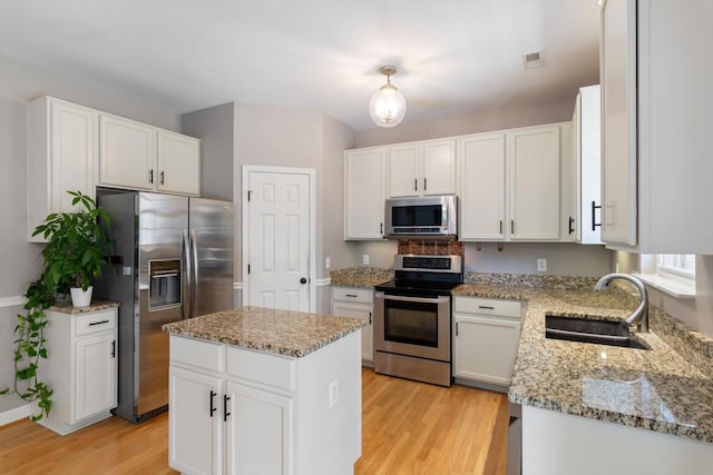 kitchen with light wood-style floors, a sink, light stone countertops, and stainless steel appliances
