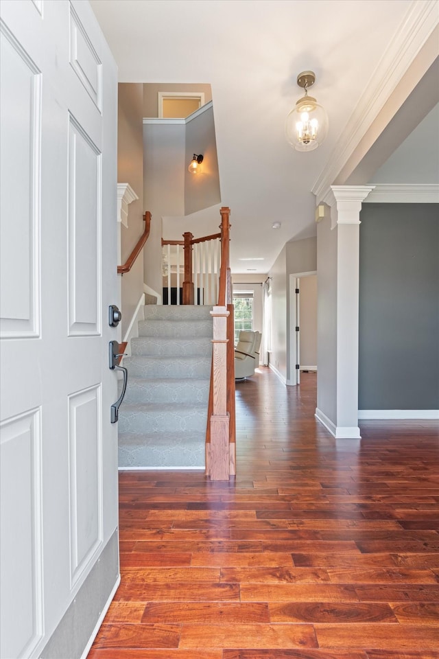 foyer entrance with stairs, baseboards, wood finished floors, ornate columns, and ornamental molding