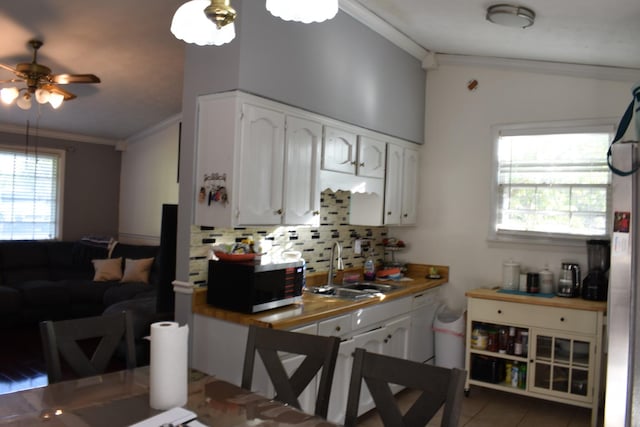kitchen with crown molding, a sink, white cabinetry, stainless steel microwave, and backsplash