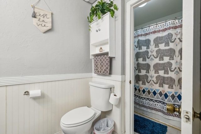 bathroom with a wainscoted wall, toilet, and curtained shower