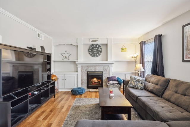 living room featuring crown molding, a warm lit fireplace, wood finished floors, and visible vents