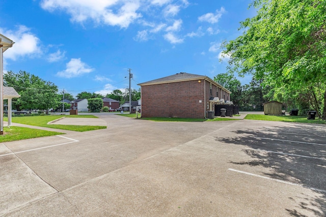 view of home's exterior with a storage unit, uncovered parking, an outbuilding, and brick siding
