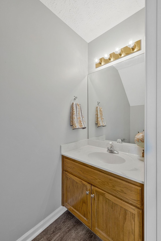 bathroom with baseboards, a textured ceiling, wood finished floors, and vanity