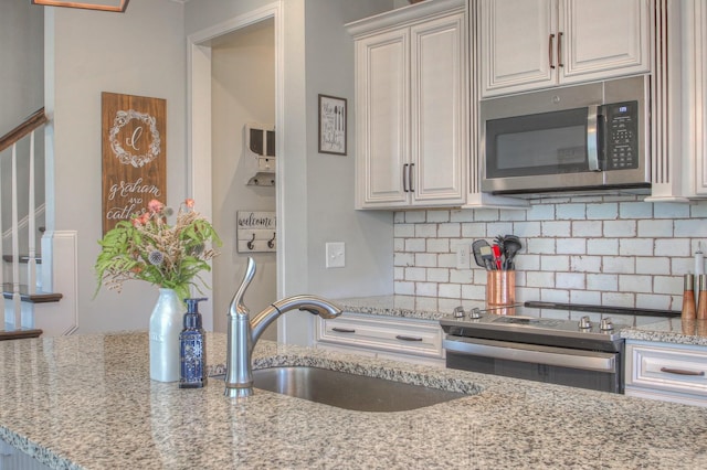 kitchen featuring a sink, tasteful backsplash, light stone countertops, and stainless steel appliances