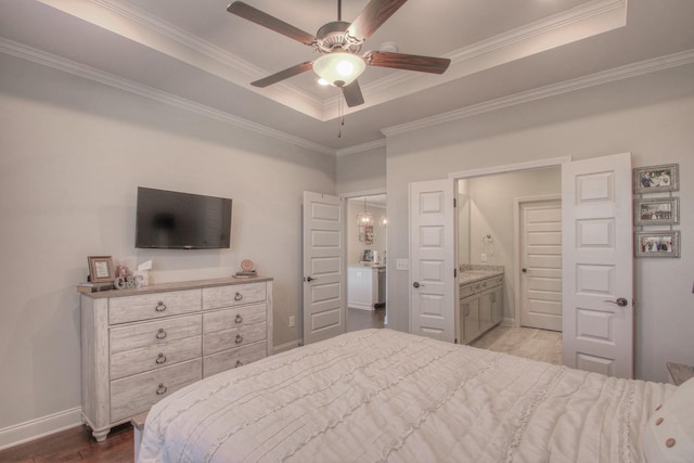 bedroom with connected bathroom, a raised ceiling, baseboards, wood finished floors, and ornamental molding