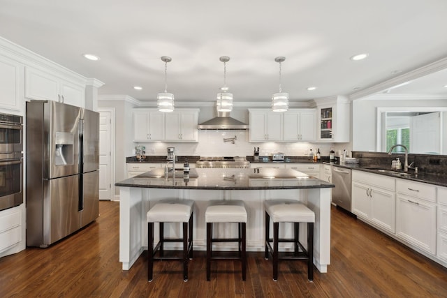 kitchen with decorative backsplash, wall chimney exhaust hood, white cabinets, a sink, and stainless steel appliances