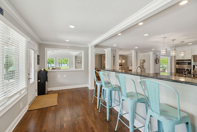 interior space with decorative columns, a kitchen bar, dark wood-style floors, dark stone counters, and recessed lighting