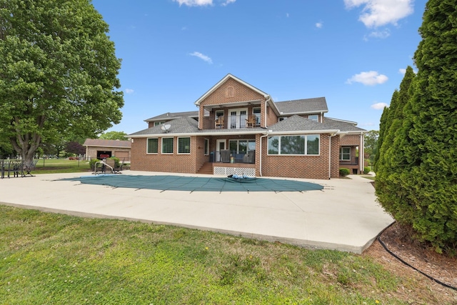 rear view of property featuring a patio, brick siding, a balcony, and a covered pool