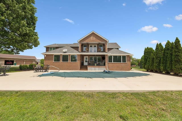 rear view of house featuring a patio, a covered pool, a balcony, and brick siding