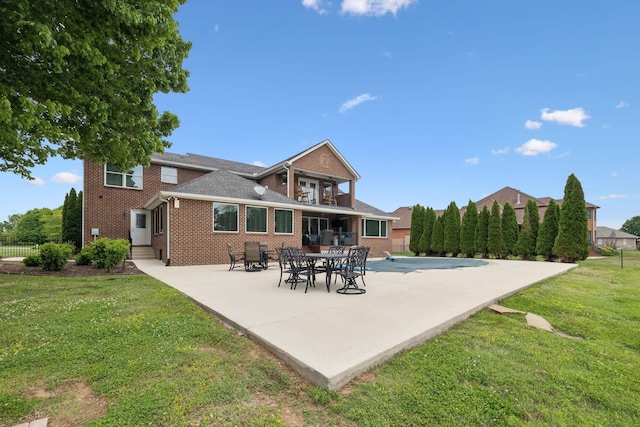 rear view of property with a lawn, brick siding, fence, a balcony, and a patio