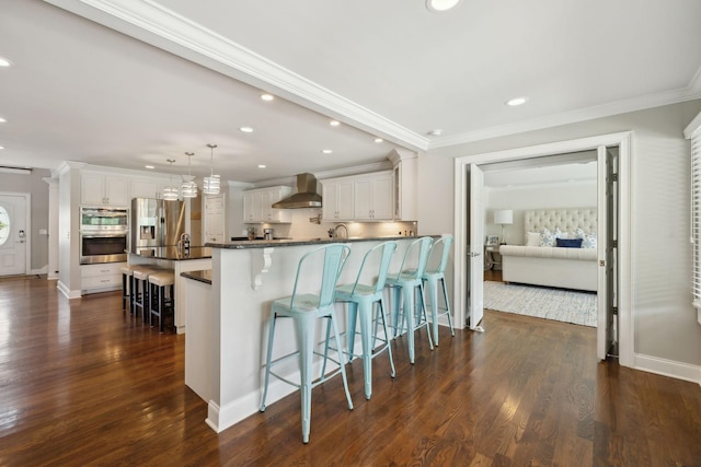 kitchen featuring wall chimney range hood, a breakfast bar area, stainless steel appliances, and recessed lighting