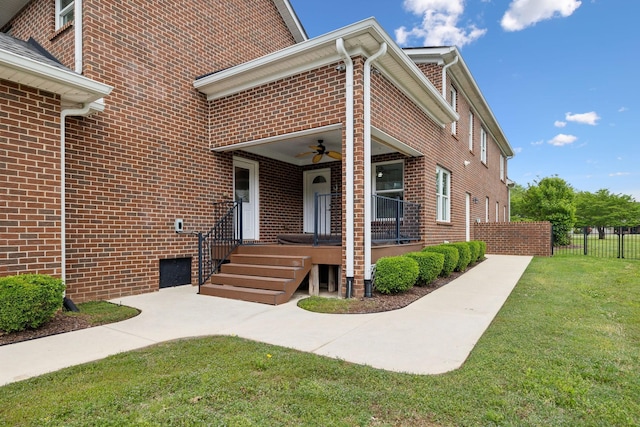 exterior space with a lawn, a ceiling fan, fence, and brick siding