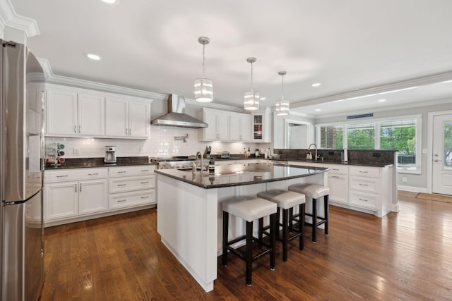 kitchen featuring wall chimney range hood, ornamental molding, freestanding refrigerator, and white cabinetry