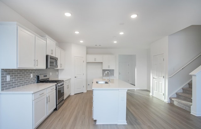kitchen with white cabinets, appliances with stainless steel finishes, a sink, light wood finished floors, and decorative backsplash