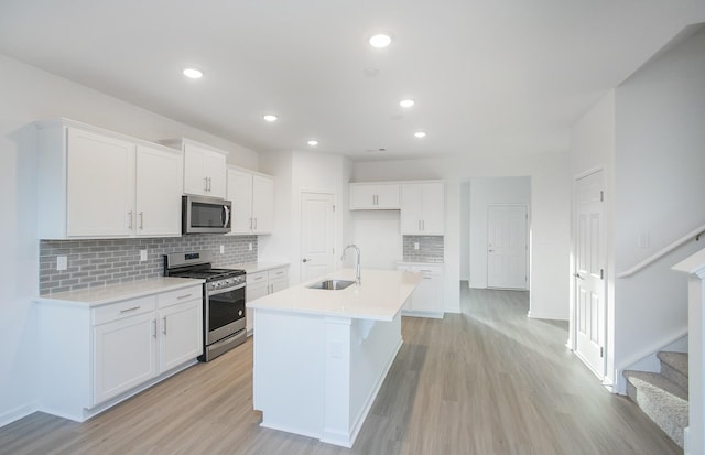 kitchen featuring white cabinets, tasteful backsplash, a sink, light wood finished floors, and stainless steel appliances