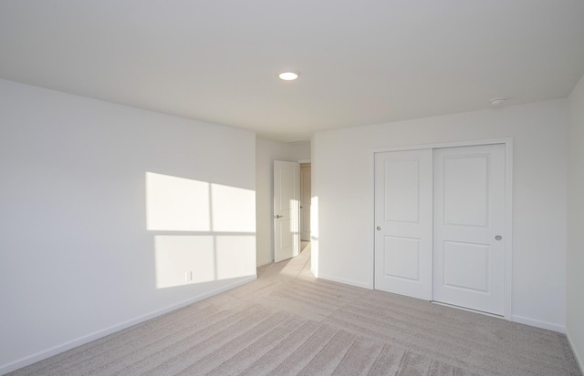 unfurnished bedroom with baseboards, light carpet, a closet, and recessed lighting
