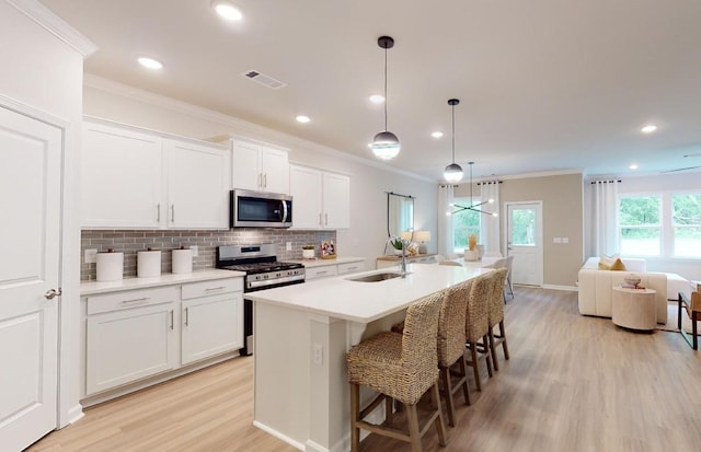 kitchen featuring visible vents, ornamental molding, a sink, light wood finished floors, and stainless steel appliances