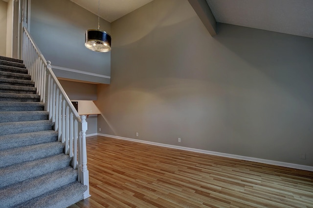 stairway featuring baseboards, a high ceiling, and wood finished floors