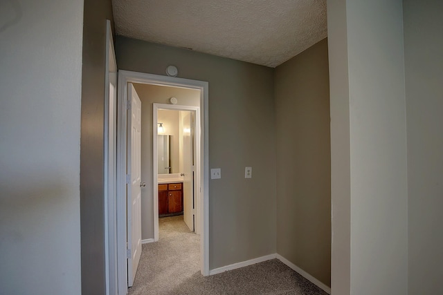 hall featuring a textured ceiling, baseboards, and light colored carpet