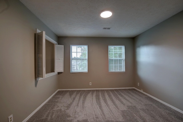 carpeted empty room featuring visible vents, a textured ceiling, and baseboards