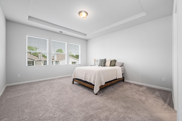carpeted bedroom with baseboards, a tray ceiling, and visible vents