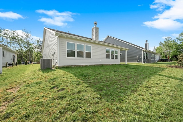 rear view of house featuring central air condition unit, a chimney, and a yard