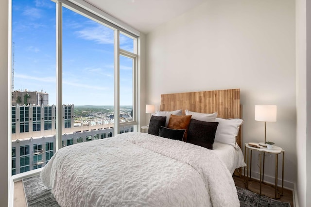 bedroom featuring a wall of windows, a view of city, and wood finished floors