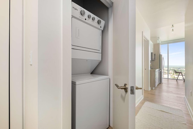 clothes washing area with baseboards, light wood finished floors, stacked washer and dryer, and laundry area